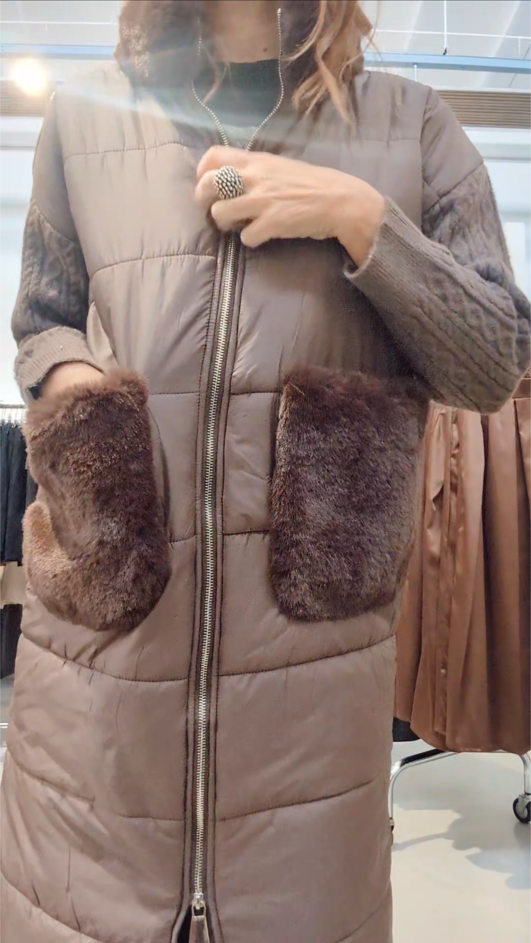 Donna che indossa un piumino lungo bianco con collo in pelliccia ecologica, maniche in maglia e tasche morbide, in negozio di abbigliamento.