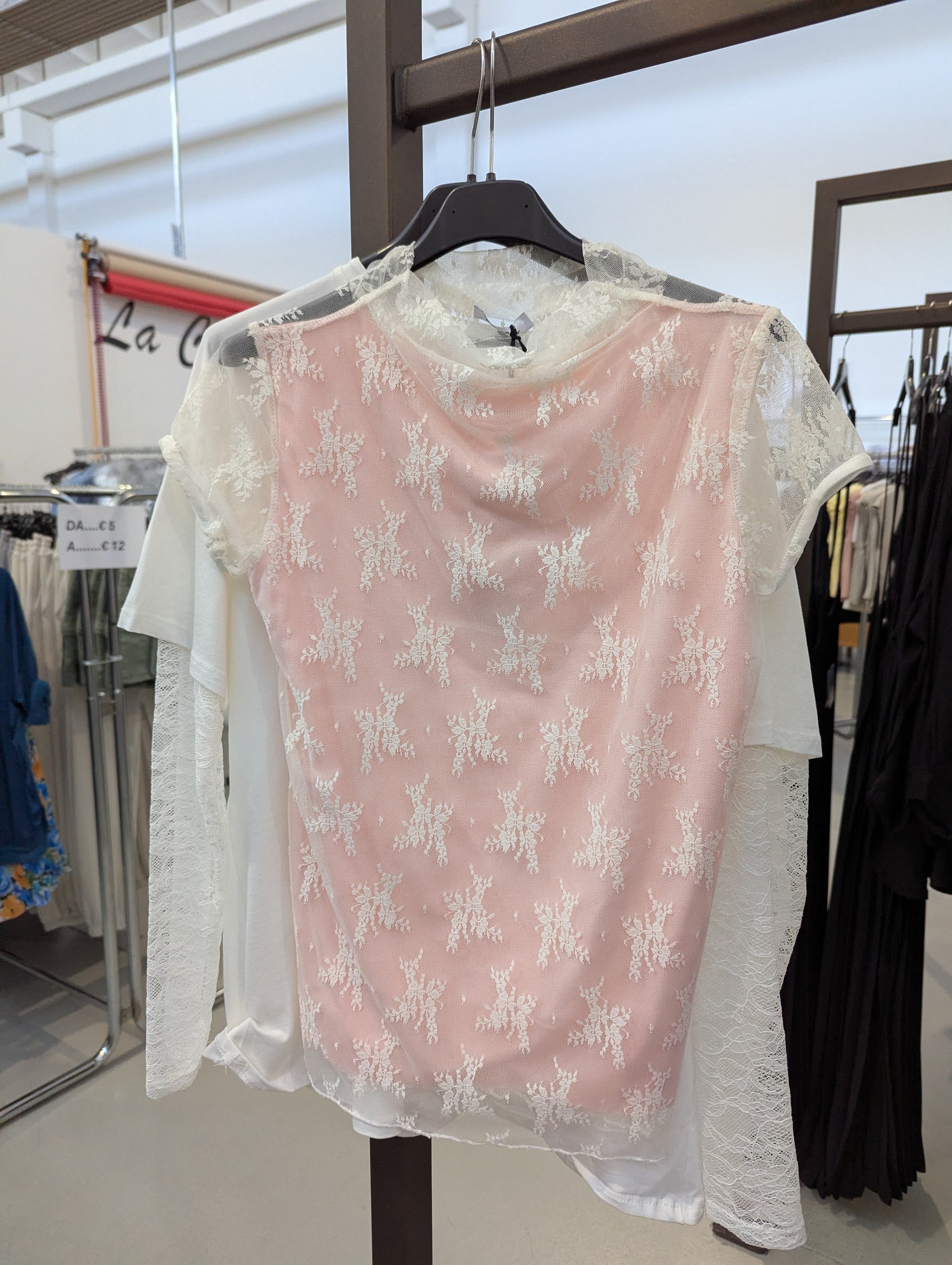 Questa maglia è davvero romantica e delicata: ha una base bianca con maniche in pizzo e un inserto rosa cipria sul davanti decorato con ricami floreali in pizzo bianco. È femminile, elegante e perfetta per la primavera o un'occasione speciale.